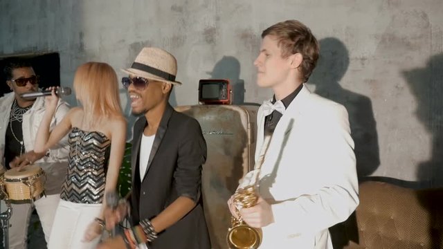 Four musicians perform in a nightclub. A beautiful white girl is dancing. A black man sings, one musician plays the saxophone, another black man plays the drums.