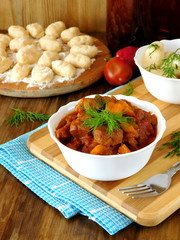 Meat stewed in tomato sauce. Porkolt, Hungarian cuisine meal. Gnocchi, a type of dumplings in the background