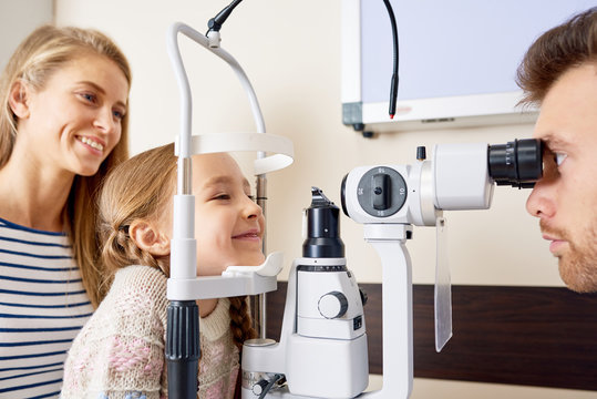 Portrait of cute little girl smiling happily looking at slit lamp machine during medical check up in eye clinic