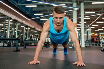 Fototapeta premium Front view portrait of handsome young man doing plank exercise while working out on floor in modern gym, copy space