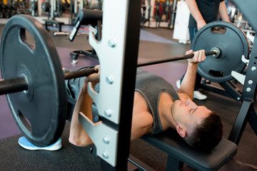 High angle portrait of handsome young sportsman lifting barbell lying on bench during weightlifting training in modern gym