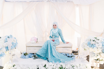 Portrait of attractive young woman in Malay or Asian traditional wedding dress sitting on bridal dais. Love and marriage concept.