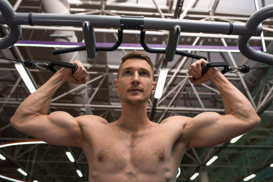 Low angle portrait of shirtless muscular man pulling up on bar during workout in modern gym