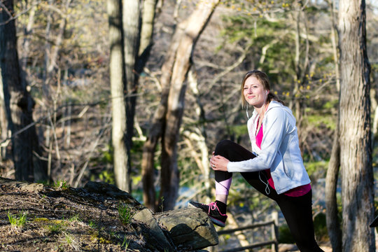 Fitness woman in the forest stretching legs before jogging
