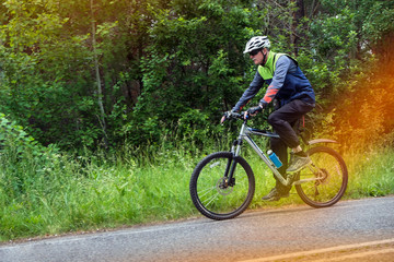 An elderly bicyclist.
A horizontal frame. A pensioner in bicycle equipment rides a bicycle against the backdrop of summer greenery.