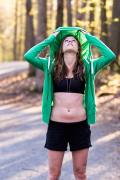 Sport lifestyle concept. Woman in sports bra pulls sweatshirt hood over her head.