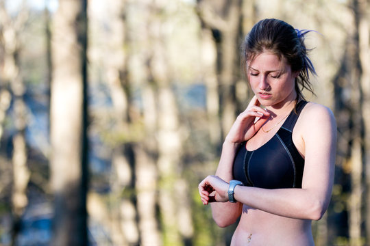 Sporty woman monitors heart rate while running in forest.