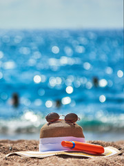 Bonnet hat, sunglasses and bottle of sunscreen against the sea.