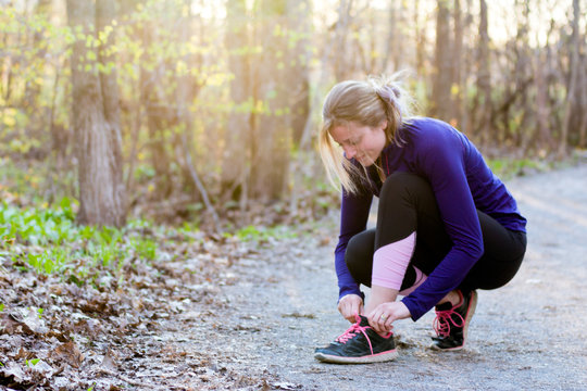 Young fitness woman runner tying shoelace in nature trail at sunset