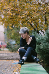 portrait of a young women sitting on a bench in park on autumn day 