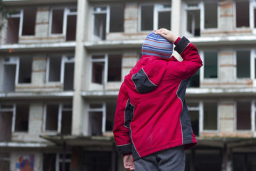 Ребенок в красной куртке смотрит на заброшенное здание