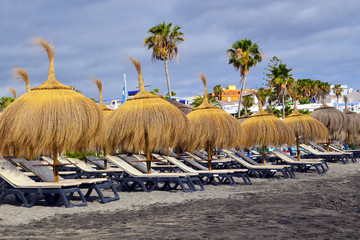 Sunbeds and straw beach umbrellas on sandy beach Playa de Torviscas in south Tenerife,Canary...