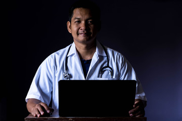 The portrait of asia doctor was sitting on the desk with use laptop.Low key style.
