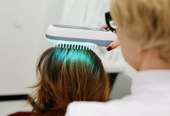 Doctor examines scalp a pretty young girl with special instrument UV lamp. Skin problems, dermatology, shingles, psoriasis, redness, prevention