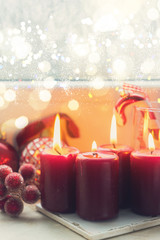Christmas styled scene with four red burning candles on windowsill with frozen window, retro toned