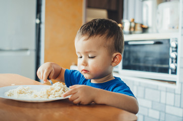 Baby in the kitchen eagerly eating pasta