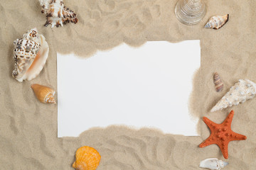 Seashells on sand with white paper in center