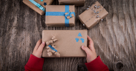 Fototapeta na wymiar Children hands holding Christmas handmade present box on rustic wooden table