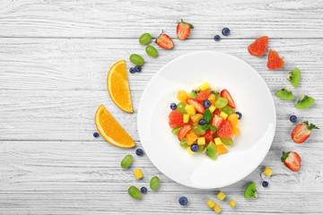 Composition with plate of fresh fruit salad on wooden table