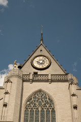 Looking up at St Peter's Church (Sint-Pieterskerk) in Leuven, Belgium. Gold clock and gold man rings the bell. Delicate tracery surrounds stained glass window. Exterior of St Peter's Church in Leuven.