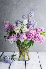 Poster lilac branches in a glass vase on a gray background © yakovlevadaria