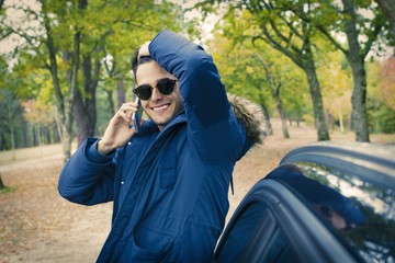 young in autumn talking on mobile phone outdoors with car