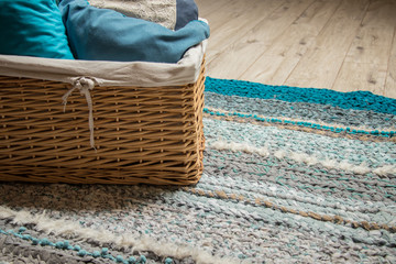 rattan basket with blue and beige pillows standing on hand made rug