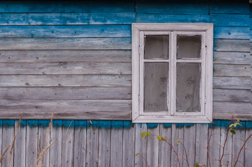 The wall of the old village house. The blue paint from the wall is blurred by time. On the wall there is a window with a curtain. Background. Texture.