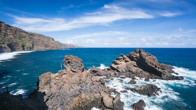 Rocks and waves at Playa de Nogales beach in La Palma, Spain with a red flag in the wind. 