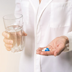 Adult woman holding pills and glass of water. Age, medicine, healthcare concept. Selective focus.