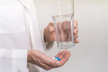 Adult woman holding pills and glass of water. Age, medicine, healthcare concept. Selective focus.