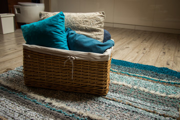 rattan basket with blue and beige pillows standing on hand made rug