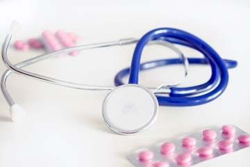 blue stethoscope and pink pills on white table in doctor's offic