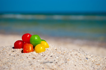 multicolored candy dragees lie on yellow sand summer beach sea shore blue sky vacation rest weekend