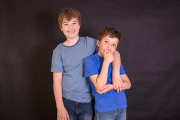 Brothers having fun whilst posing. Boys portrait, young little cute and adorable kids, little obstreperous scamps. Poses, face expressions, ease,  black background.