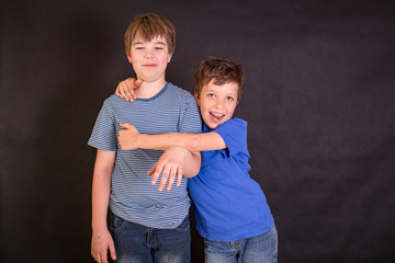 Brothers having fun whilst posing. Boys portrait, young little cute and adorable kids, little obstreperous scamps. Poses, face expressions, ease,  black background. - obrazy, fototapety, plakaty