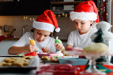 Two happy children decorating cookies for holidays at home