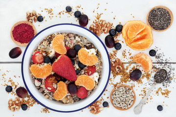 Healthy food for breakfast including granola, fresh fruit, nuts, pollen grain, yoghurt, acai berry powder and chia seed with foods high in omega 3, protein, antioxidants, anthocyanins and vitamins.
