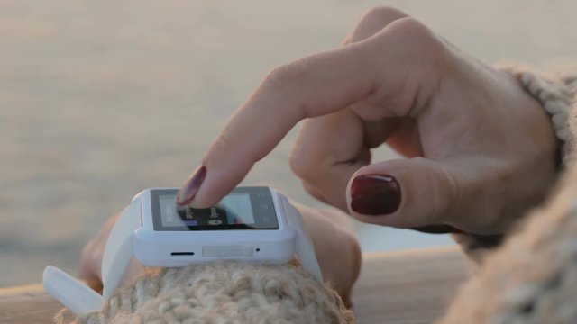 Woman using wearable smartwatch computer device on deck of cruise ship at sunset. Sunset light, golden hour. Technology and journey concept