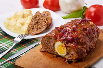 Traditional Cuban meatloaf pulpeta with an egg in the middle. Delicious, hearty lunch. Mashed potatoes with a large meat roll. Fresh vegetables in the background.