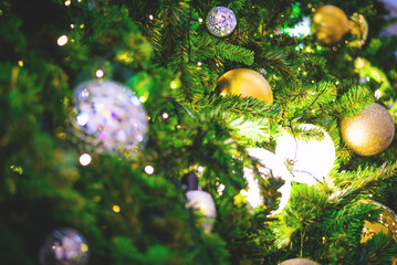 Closeup and selective focus of golden and silver bauble hanging from a decorated Christmas tree with beautiful light and bokeh