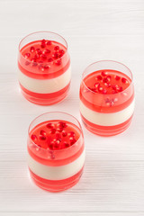 Creamy vanilla panna cotta with red jelly in beautiful glasses, fresh ripe pomegranate on white wooden background.