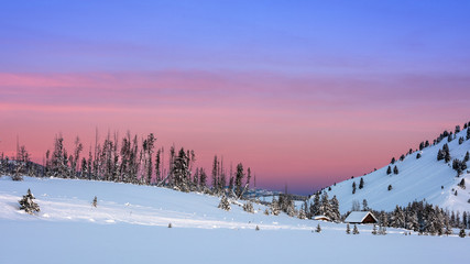Sky colored with hues of morning over a snow covered field with cabin