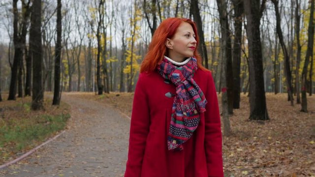Red hair young woman in coat happy walks in autumn park