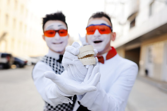 Two mimes in dental glasses are holding a cast of the jaw in their hands. Dental prosthetics