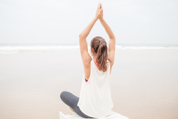 Fototapeta na wymiar Woman practices yoga at the seashore on overcast day