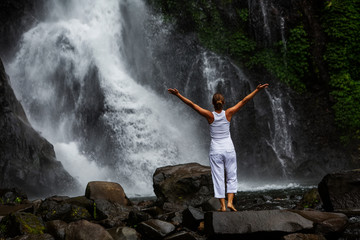 Obraz premium Woman practices yoga at Gitgit waterfall on Bali in indonesia