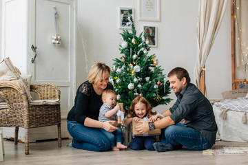 Young happy family of four having fun near christmas tree. Happy new year concept. Cheerful parents and kids