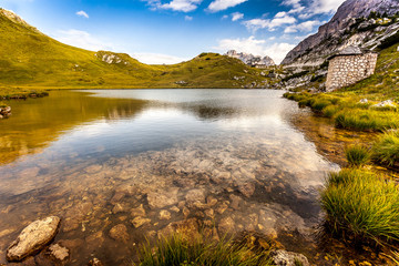 Fototapeta na wymiar Small dolomitic crystalline lake with mountain hut background, Valparola Pass, Dolomites, Italy