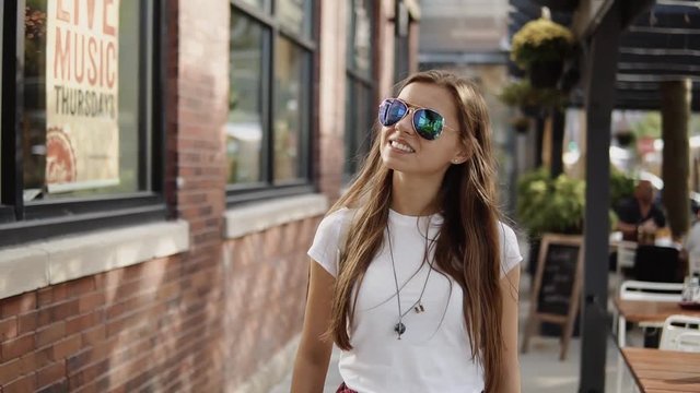 beautiful smiling girl in fashion sunglasses stands near the entrance to city street cafe